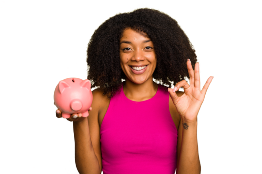 Young African American woman holding a piggy bank isolated cheerful and confident showing ok gesture.