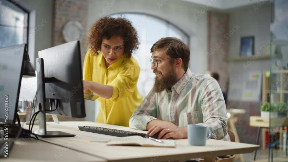 Poster Portrait of Two Creative Colleagues Collaborating and Pointing at the Computer Screen in Modern Bright Office. Biracial Young Woman Discussing Work with Caucasian Male Assistant. Slow Motion.
