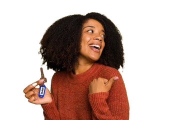 Young African american woman holding home keys isolated points with thumb finger away, laughing and carefree.