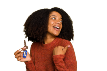 Young African american woman holding home keys isolated points with thumb finger away, laughing and carefree.