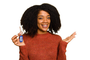 Young African american woman holding home keys isolated showing a copy space on a palm and holding another hand on waist.