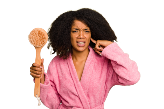 Young African American woman holding a shower brush isolated covering ears with hands.