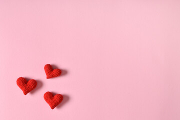Three red knitted hearts on a pink background.