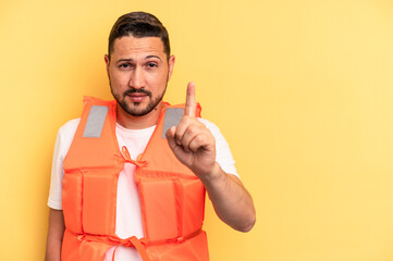 Young latin beach watcher wearing a lifejacket isolated showing number one with finger.