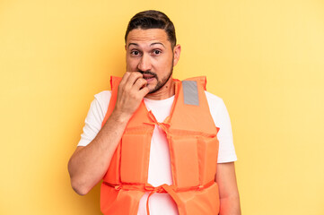Young latin beach watcher wearing a lifejacket isolated biting fingernails, nervous and very...