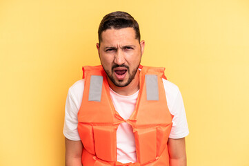 Young latin beach watcher wearing a lifejacket isolated screaming very angry and aggressive.