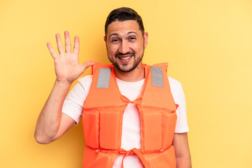 Young latin beach watcher wearing a lifejacket isolated smiling cheerful showing number five with...