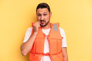 Young latin beach watcher wearing a lifejacket isolated with fingers on lips keeping a secret.