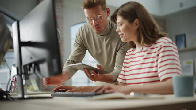 Two Creative Colleagues Discussing and Pointing at the Computer in Modern Bright Office. Caucasian Male Sales Manager Discussing Project Plan with White Female Legal Assistant. Slow Motion.