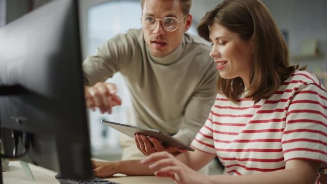 Portrait of Two Creative Colleagues Using Computer and Tablet to Discuss Work Project. Young Caucasian Technical Support Specialist Helping Female Customer Relationship Coordinator. Teamwork Concept