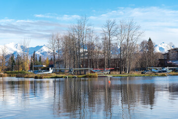 Seaplanes at the base on Lake Spenard with snow cap Chugach Mountain and row of dormant trees in early fall in Anchorage, Alaska