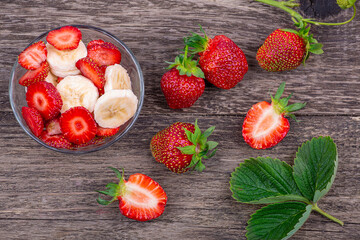 Fresh strawberries, a plate with sliced strawberries and a banana, on a wooden background