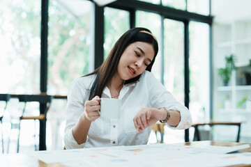 A portrait of a beautiful Asian employee hustle rushing while watch at the clock and talking on the...