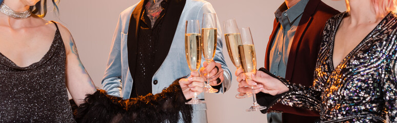 partial view of stylish nonbinary friends clinking champagne glasses on grey background, banner