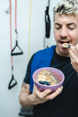 Caucasian man eating granola and smoothie bowl after training and workout at home. Fitness and healthy lifestyle concept