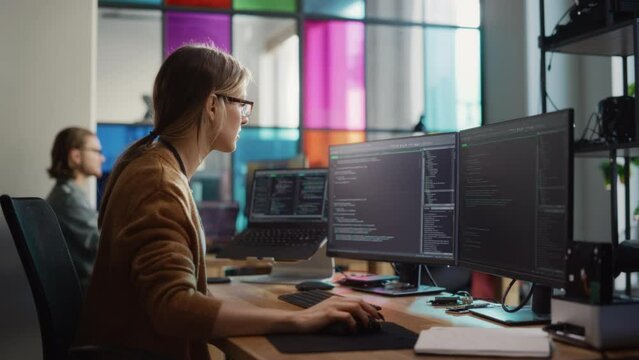 Female Software Engineer Writing Code on Desktop Computer with Multiple Screens Setup in Stylish Coworking Office Space. Professional Caucasian Woman Working on SaaS Platform For Innovative Startup.
