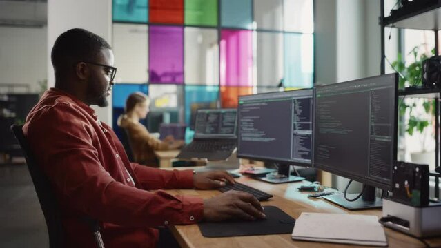 African American Man Coding on Desktop Computer with Professional Multiple Monitors Setup in Creative Office. Male Software Engineer Developing Mobile Application for Innovative Start-Up Company.