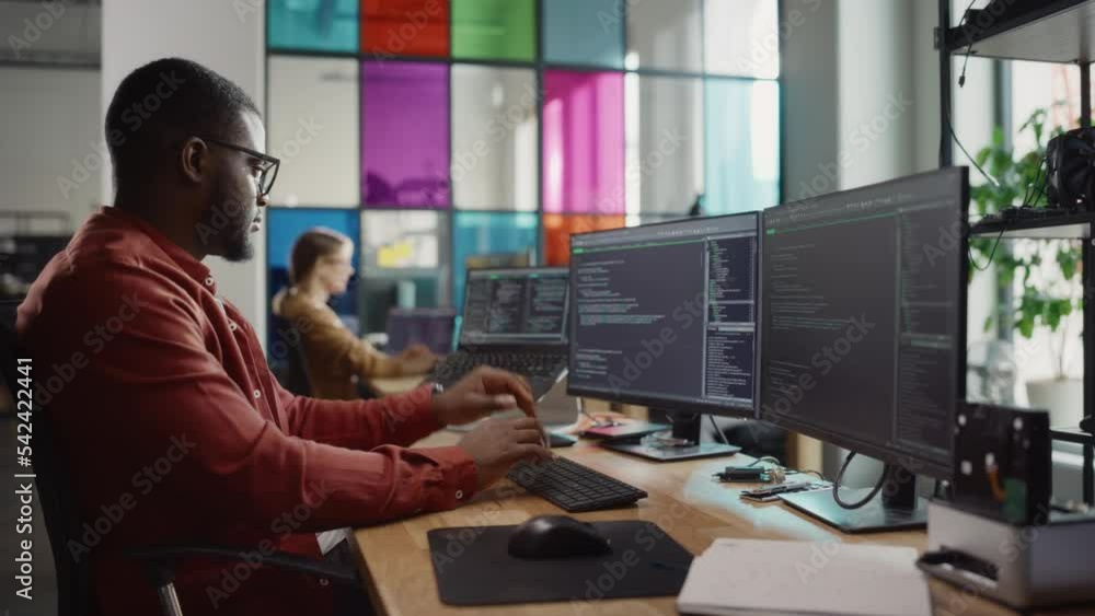 Poster Black Man Writing Lines of Code On Desktop PC With Two Monitors and a Laptop Aside in Stylish Office. Professional Male Developer Programming Artificial Inteligence Software for Start-Up Company.