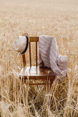 a hat, a wooden chair, a plaid, a shawl stand in the middle of a ripe wheat field