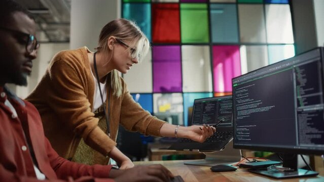 Female Team Lead Gives Advice to Black Junior Developer, Pointing at Desktop Computer Display in Creative Office Space. Caucasian Woman Offering Useful Coding Hacks To Male Software Engineer.
