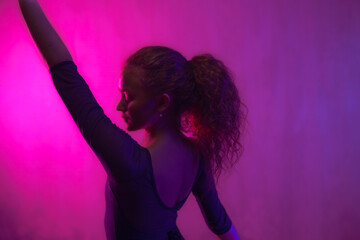 Ballet girl dancer dancing in neon light doing gymnastic exercises in studio, copy space. © Halfpoint