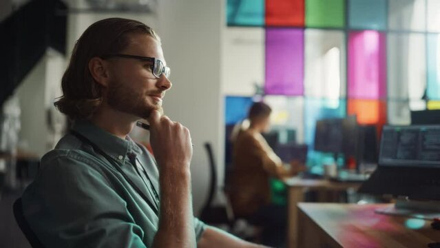 Caucasian Man Comes Up With Idea And Starts to Write Code on Desktop Computer with Two Monitors in Creative Office. Succesful Male Software Engineer Fixing A Bug in Mobile App for Online Service.