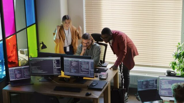 Diverse Developers Looking at Desktop Computer Monitor in Creative Office. Black Man and Caucasian Woman Helped Software Engineer Team Member to Fix a Bug. Successful Programmers High Five Each Other