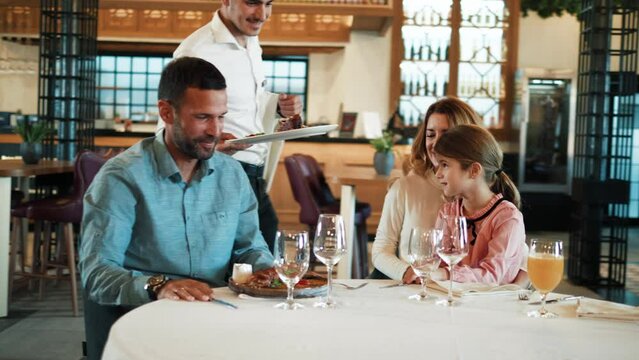 A waiter serves food on a table to a happy family in a restaurant