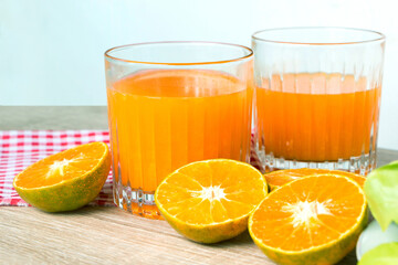 Glass of fresh tangerine juice and orange slice on wood table.