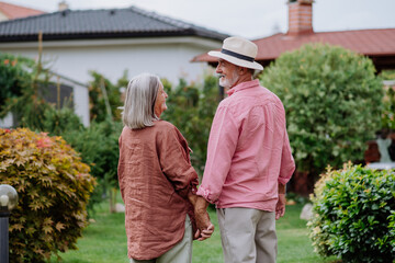 Rear view of senior couple posing together in their garden, holding each other hands.