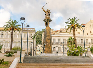 Fototapeta na wymiar El Amir Abdelkader statue with flying pigeons and palm trees in Emir abdelkader place, Larbi Ben M'hidi and Colonel Haouas road. Algiers city town hall building. Stairs, posts, trees and cloudy sky.