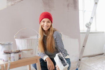 Happy young woman remaking her new flat, painting walls. Concept of renovation, indepent women and sustainable lifestyle.