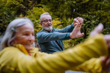 Happy senior couple doing stretching during hiking in autumn forest.