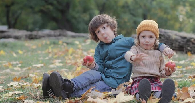 little brother and sister sitting in the park eat apples and enjoy a good day. Children hug, laugh and have fun