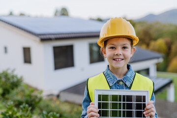 Little girl with protective helmet and reflective vest holding photovoltaics solar panel....