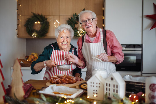 Happy seniors baking together Christmas cakes in their kitchen.
