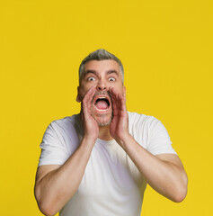 Handsome grey haired man cover his mouth with hands to help send sound wearing white t-shirt...
