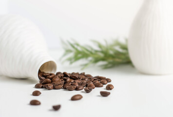Coffee beans spilled on white with greenery in the background