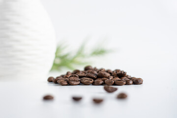 Coffee beans spilled on white with greenery in the background