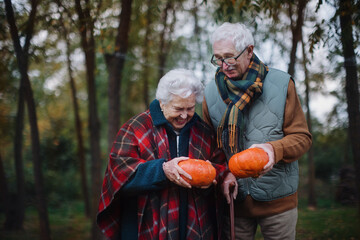 Senior couple with pumpkins in autumn forest.