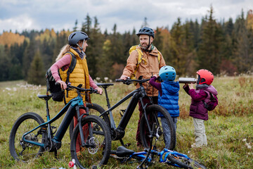 Young family with little children preparing for bicycle ride in nature, putting off bicycles from car racks. Healthy lifestyle concept.