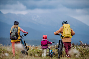 Rear view of family with little child at bicycles, in the middle of autumn nature.Concept of a...