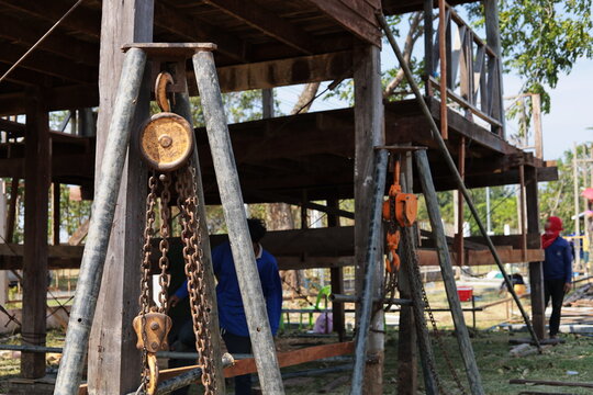 Chain hoist lifting wooden pole. An old chain hoist system on a tripod straps and supports ancient wooden house poles to raise the height to prevent flooding in shallow view with copy space.
