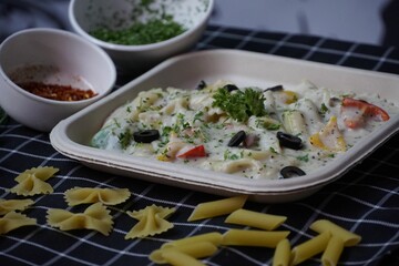 Closeup shot of a lunchbox with a dish in it and pasta on the tablecloth