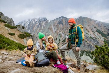Happy family resting, having snack during hiking together in autumn mountains.