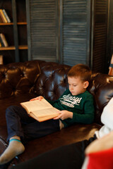 Boy reading a book sitting on a sofa on a dark background
