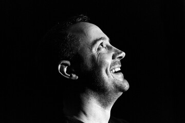 Laughing happy man low key portrait in black and white silhouette in profile looking upwards