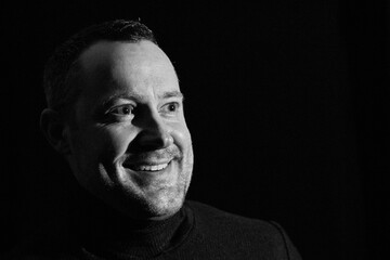 Smiling nice man with shining eyes and turtleneck sweater in the low key picture black and white profile
