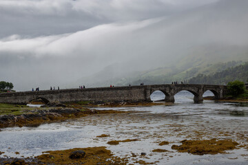 Tourists passing through the stone bridge of Eilean Donan Castle in the Highlands of Scotland