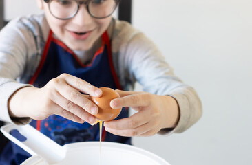 Exited boy cooking cookies at home close-up breaking egg